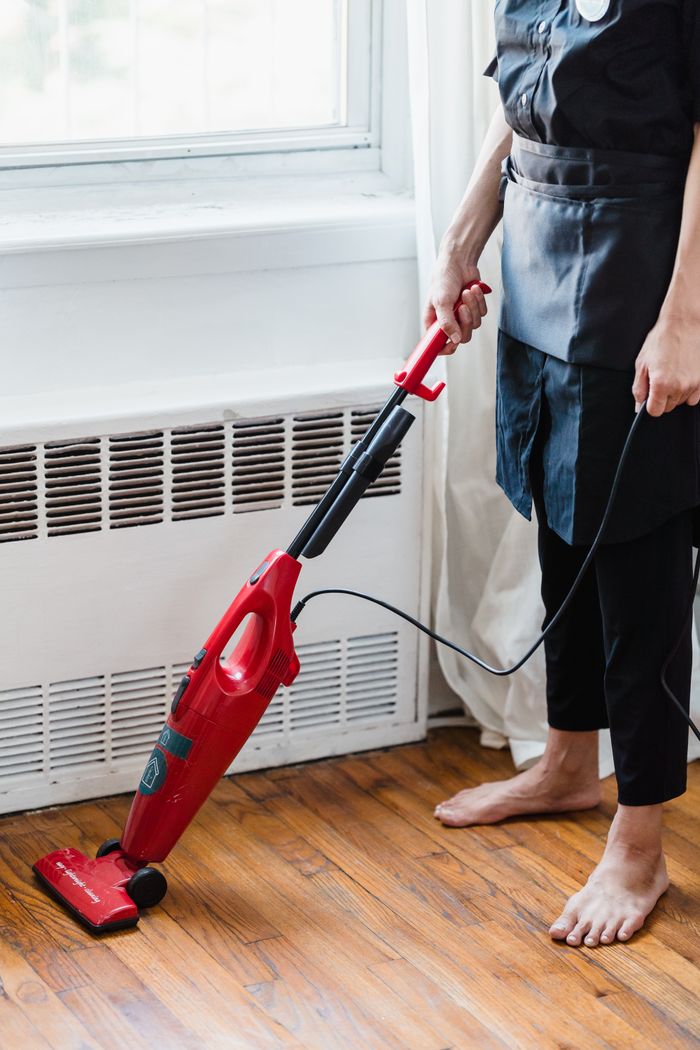 mobile-01 Person cleaning wooden floor with red vacuum cleaner in a well-lit room.